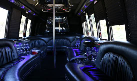 Party bus interior with black leather seating, purple accent lighting, and a central dance pole.
