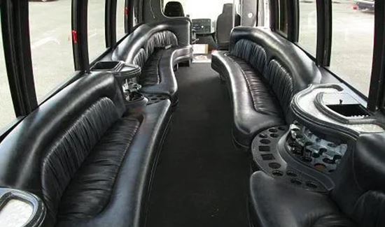 Party bus interior with curved black leather seating, built-in cup holders, and large windows.