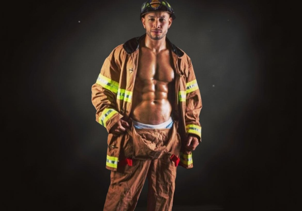 Muscular man in firefighter-themed outfit, posing seductively.