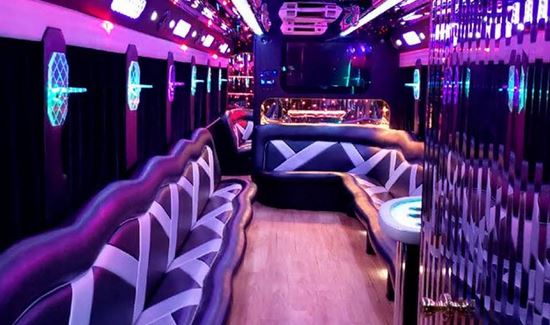 Vibrant party bus interior with purple and blue neon lighting, sleek patterned leather couches, and a club atmosphere.