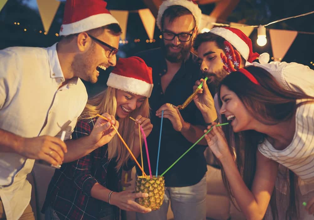 Christmas party group laughing and drinking a tropical cocktail with straws from a pineapple.