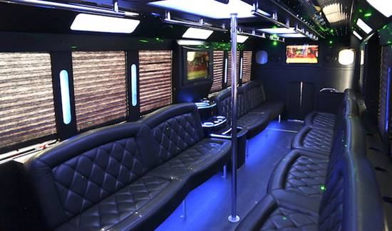 Interior of a luxury party bus with leather seating on both sides, blue lighting, and a dance pole.