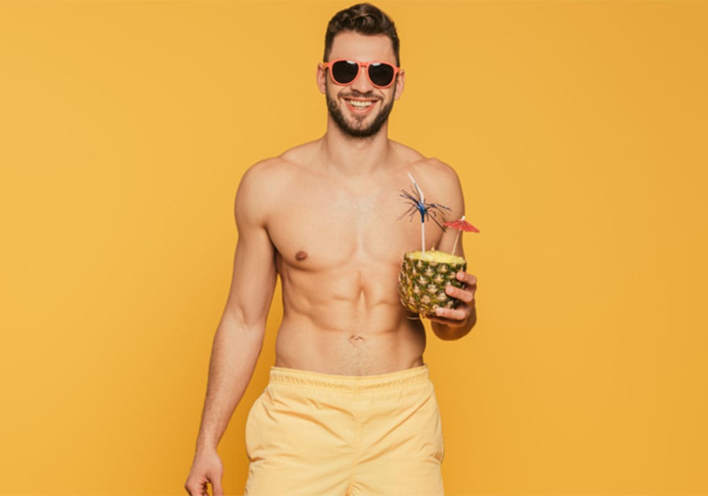 Sexy guy with a cheeky smile holding a cocktail wearing yellow shorts.