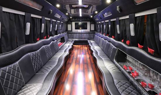 Spacious luxury party bus interior with black leather seating, rich wood flooring, and elegant accent lighting.