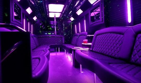Limo bus interior glowing with purple lights, quilted leather seating, and a dance pole.