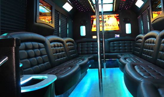 Interior of a luxury party bus with black leather couches, blue neon lights, and metal dance poles.