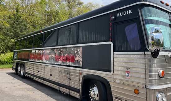 Silver and black Big City Party Bus parked near trees, with a red and white banner along the side.