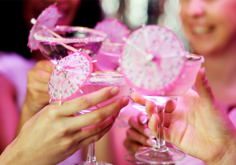 Women toasting with pink cocktails served in glasses with small pink umbrellas.