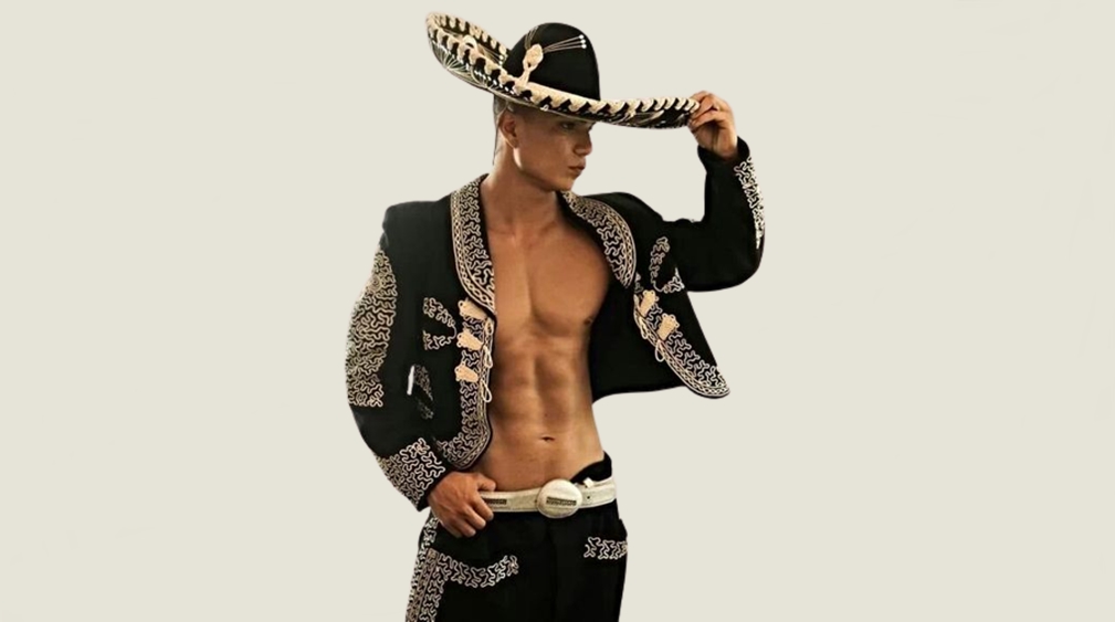 Fit male stripper in Latin Lover-style charro costume, confidently posing with one hand on his sombrero.