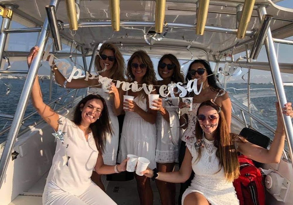 Group of women dressed in white enjoying drinks on a pontoon boat.