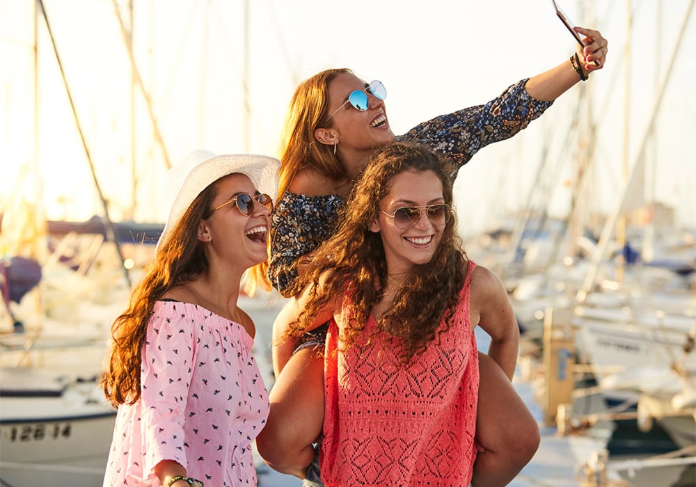 Three women taking a group selfie in a yacht harbor.