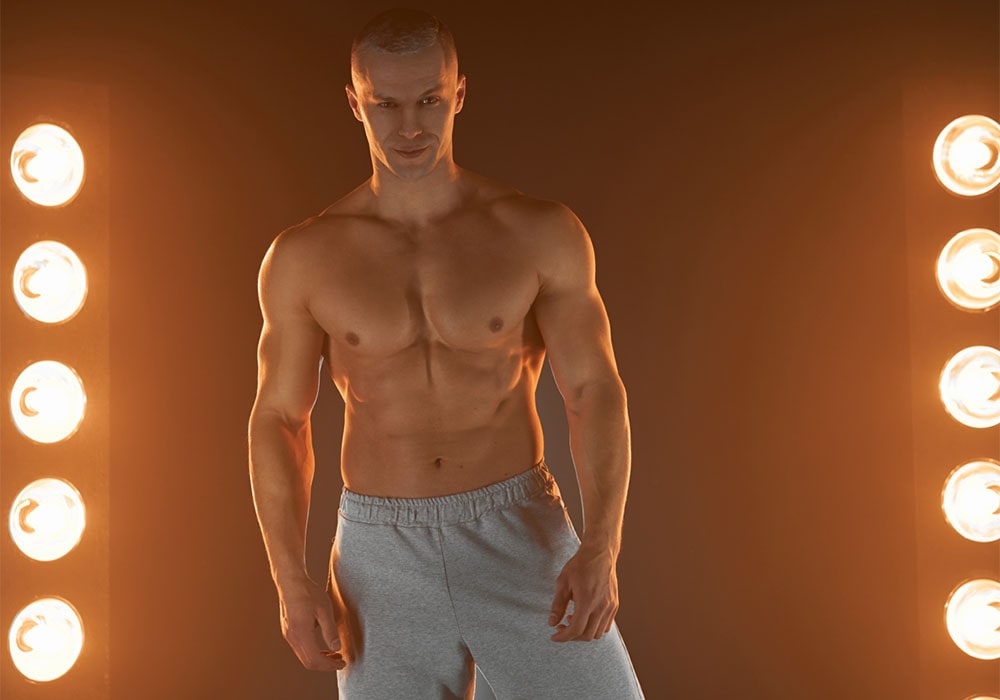 Attractive muscular guy wearing only sports pants posing near spotlights.