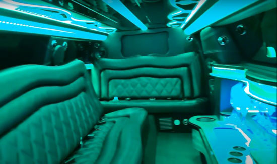 Party bus interior with leather seating, green accent lighting, and built-in drink stations.