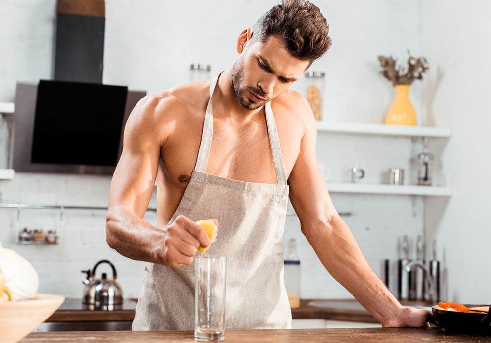 Young handsome man wearing only an apron making lemonade in the kitchen.