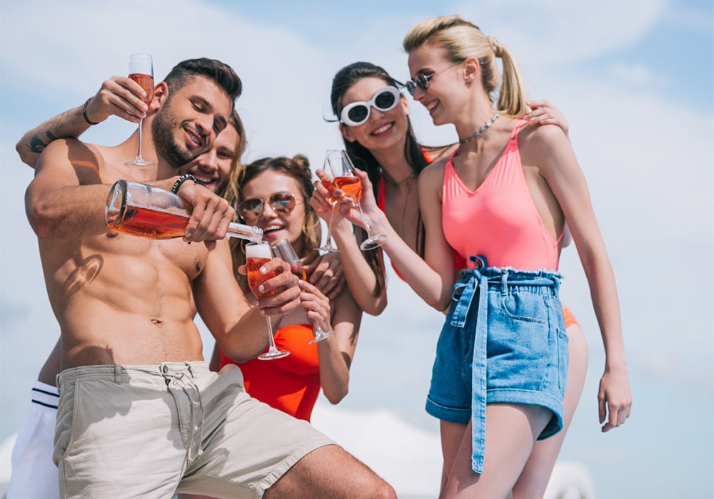 Shirtless guy pouring wine for a group of women at an outdoor party.