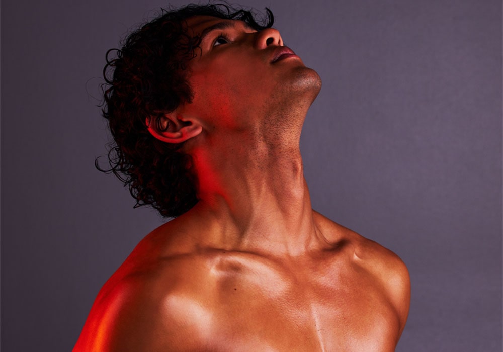 Shirtless Bad Boy stripper posing seductively in a dark setting with red lighting.