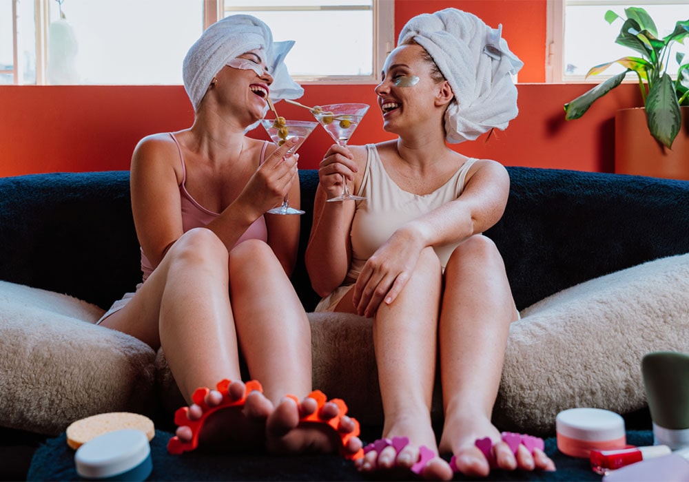 Two joyful women toasting with martinis at a pampering party.