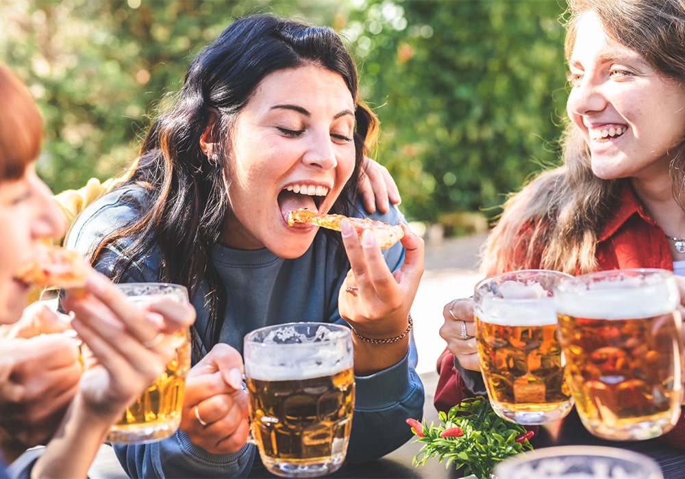 Group of joyful women eating and toasting with beer mugs at an Oktoberfest party.